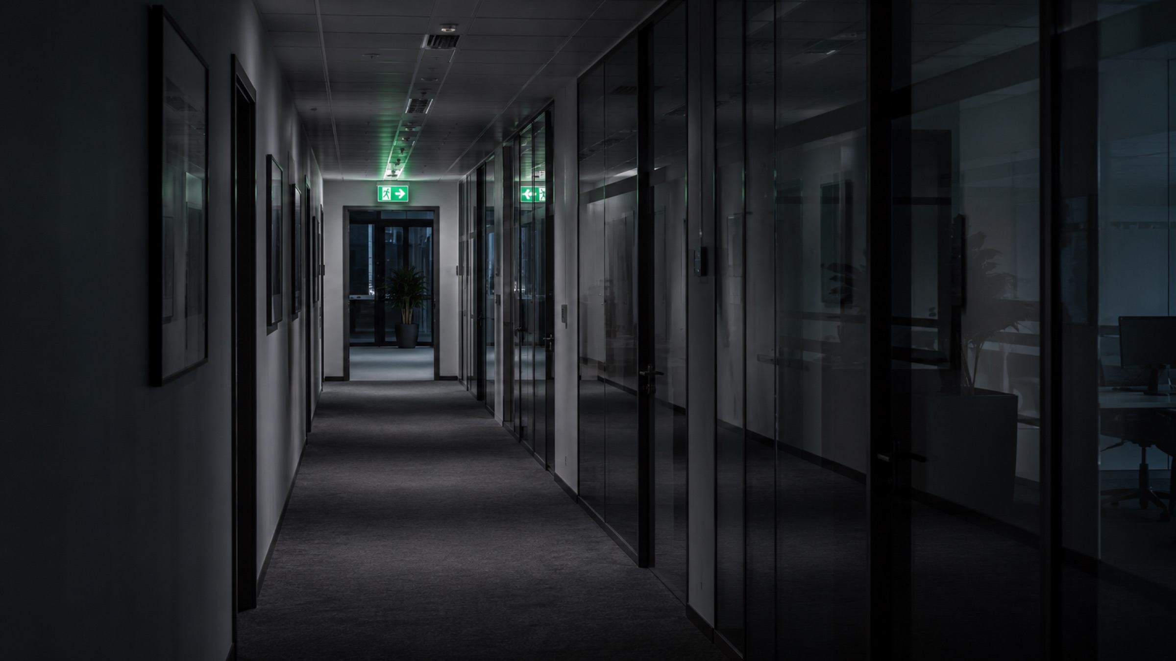 Abgedunkelter Büroflur mit Glaswänden und zwei beleuchteten Rettungszeichen